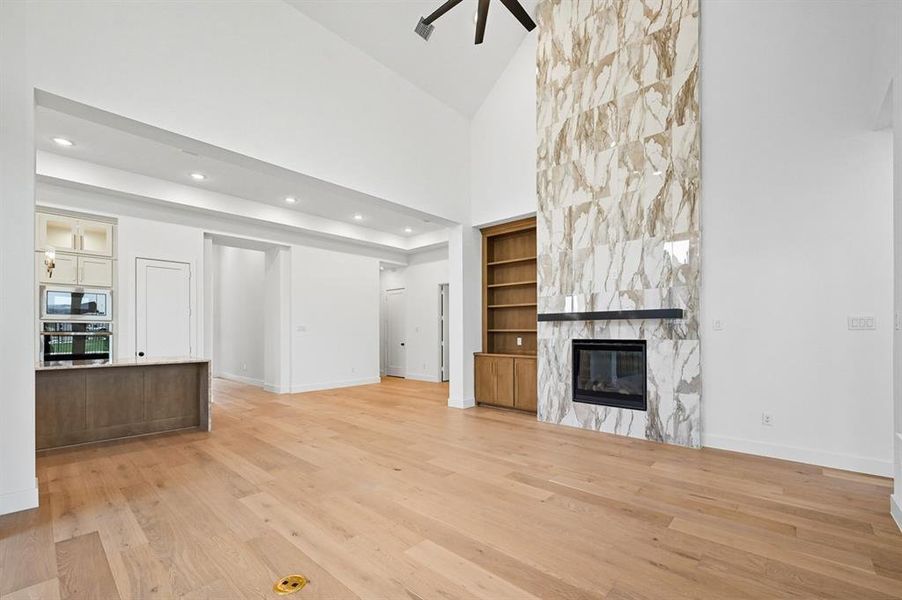 Unfurnished living room with high vaulted ceiling, light wood finished floors, a premium fireplace, built in features, and recessed lighting Unfurnished living room with high vaulted ceiling, light wood finished floors, a premium fireplace, built in features, and recessed lighting