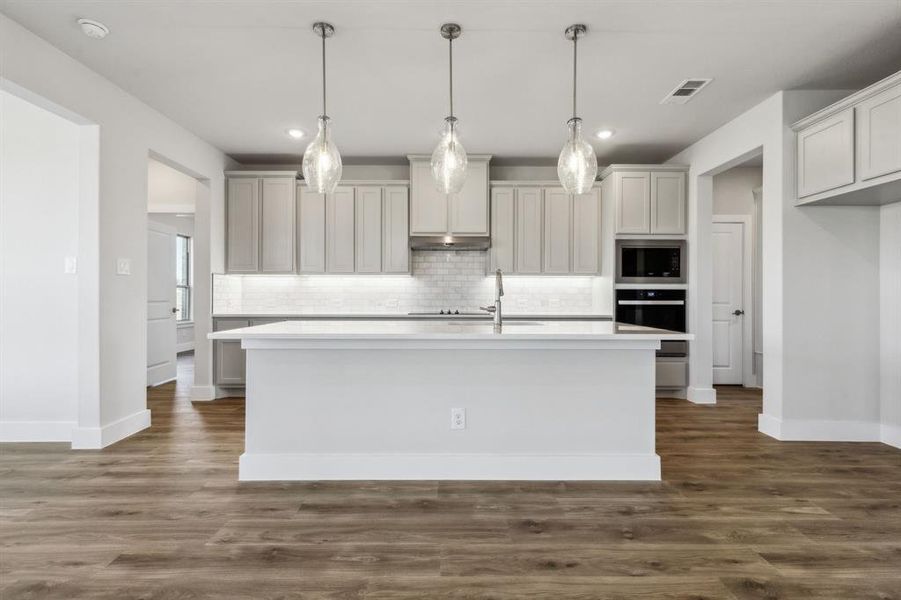 Kitchen featuring built in microwave, decorative light fixtures, oven, and a kitchen island with sink