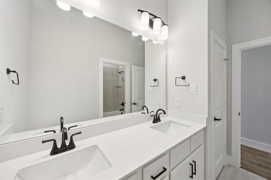 Bathroom with shower / washtub combination, double vanity, and light wood finished floors