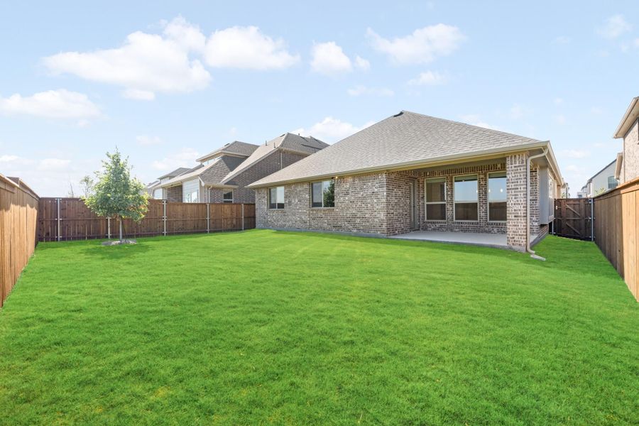 Backyard of brick home with large green lawn, covered patio, and wood privacy fence
