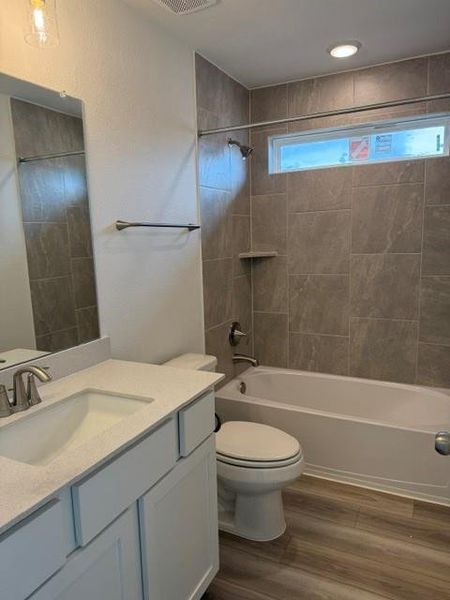 Contemporary bathroom featuring a white vanity with an integrated sink and light-toned countertop, a toilet, and a bathtub with a shower surround