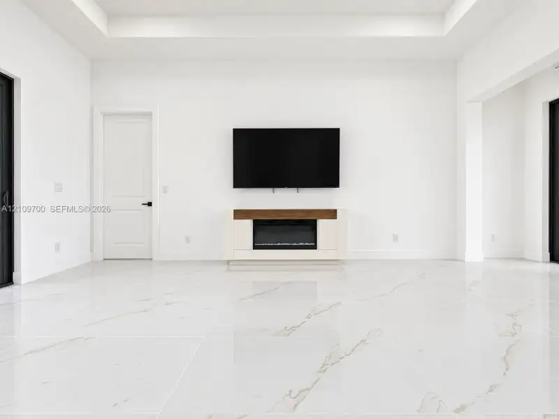 Large-format tile flooring with light veining, tray ceiling, built-in electric fireplace with wood-tone mantle, and solid-core interior doors