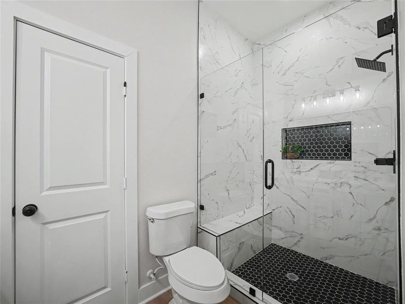 Walk-in shower featuring white marbled tile, black hexagonal floor tile, a built-in bench, and a recessed niche with accent tiling Walk-in shower featuring white marbled tile, black hexagonal floor tile, a built-in bench, and a recessed niche with accent tiling