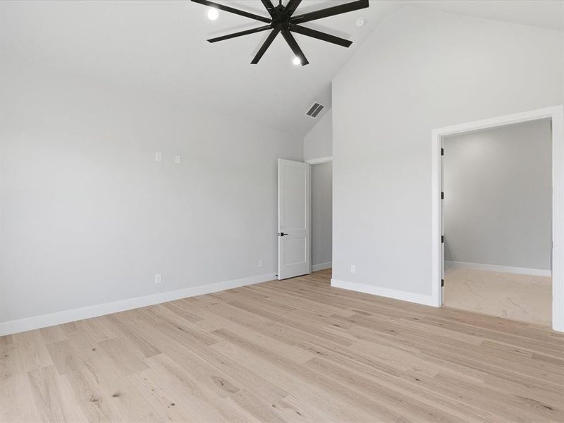 Spacious room featuring vaulted ceilings, light wood-finish flooring, and white baseboards