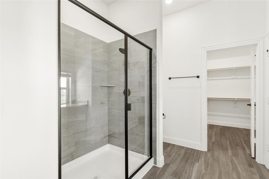 Walk-in shower with black frame glass doors and gray tile walls, adjacent to a walk-in closet with built-in shelving. Walk-in shower with black frame glass doors and gray tile walls, adjacent to a walk-in closet with built-in shelving.