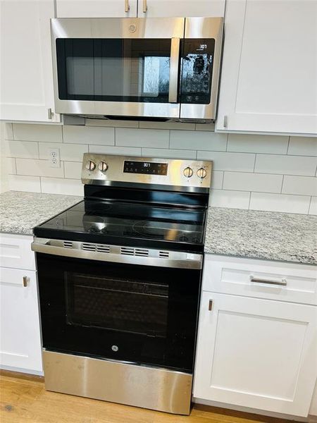 Kitchen with white cabinets, light wood-type flooring, appliances with stainless steel finishes, tasteful backsplash, and light stone counters