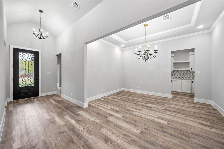 Entrance foyer with a chandelier, light wood-type flooring, a raised ceiling, and ornamental molding