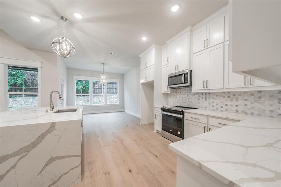 Kitchen featuring light stone countertops, appliances with stainless steel finishes, light wood-type flooring, hanging light fixtures, and white cabinets