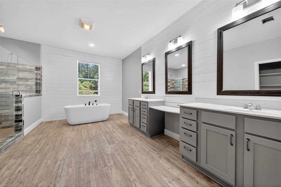 Full bath with light wood-style flooring, wooden walls, a stall shower, two vanities, and a soaking tub