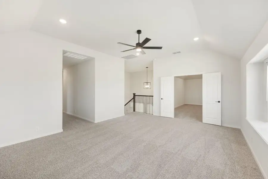 Spacious upstairs loft with carpet, vaulted ceiling, ceiling fan, and staircase landing nearby