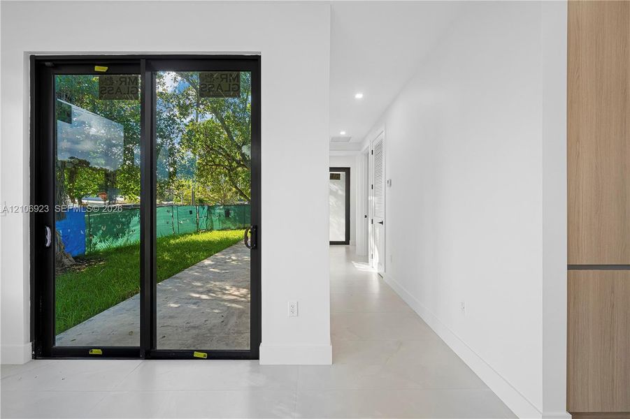 Black-framed sliding glass doors, neutral tile flooring, recessed ceiling lighting, and wood-finish cabinetry Black-framed sliding glass doors, neutral tile flooring, recessed ceiling lighting, and wood-finish cabinetry