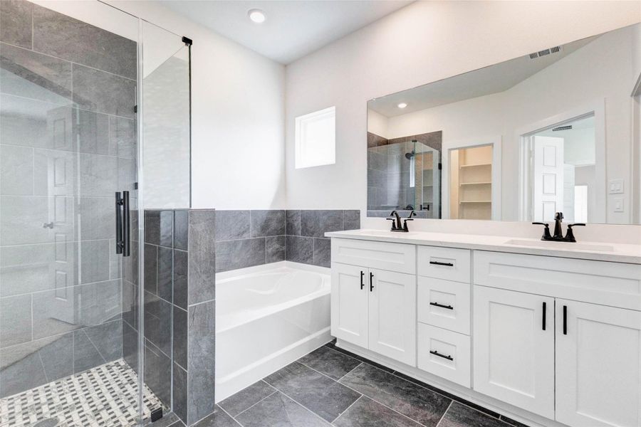 Step into a spa-inspired primary bathroom featuring a sleek double vanity with quartz countertops, modern black fixtures, and ample storage. The soaking tub is framed by elegant tile work, creating a relaxing retreat, while the oversized mirror enhances light and space. Clean lines and high-end finishes bring a sense of luxury to everyday routines.