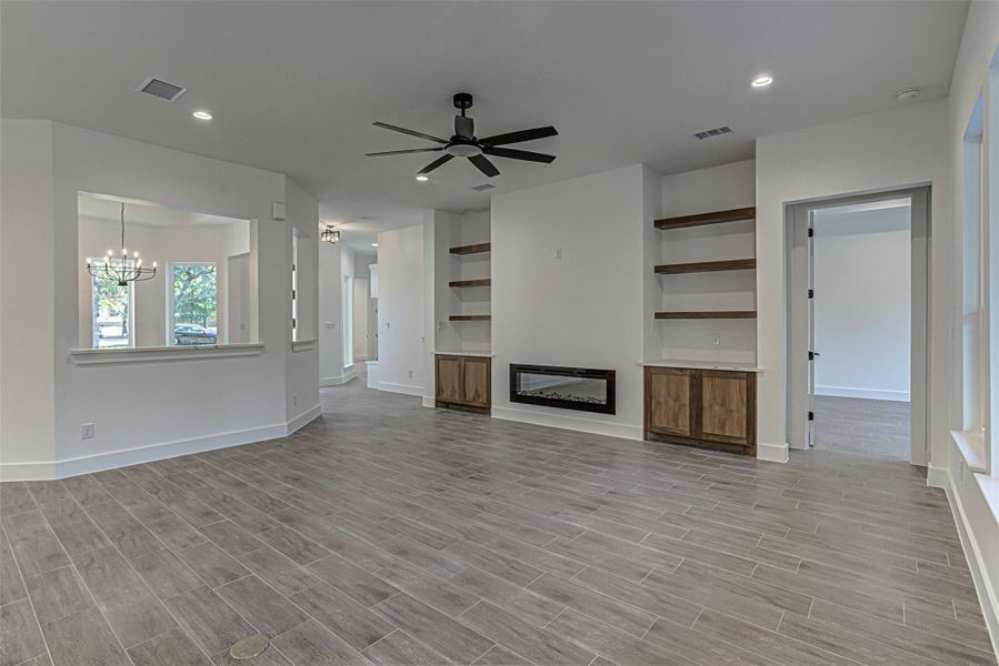 Living room featuring built in shelves, ceiling fan, electric fireplace, wood finish tiled floors Living room featuring built in shelves, ceiling fan, electric fireplace, wood finish tiled floors