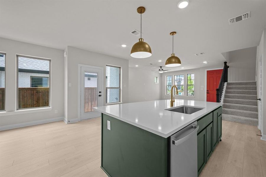 Kitchen with green cabinetry, open floor plan, an island with sink, stainless steel dishwasher, and a ceiling fan