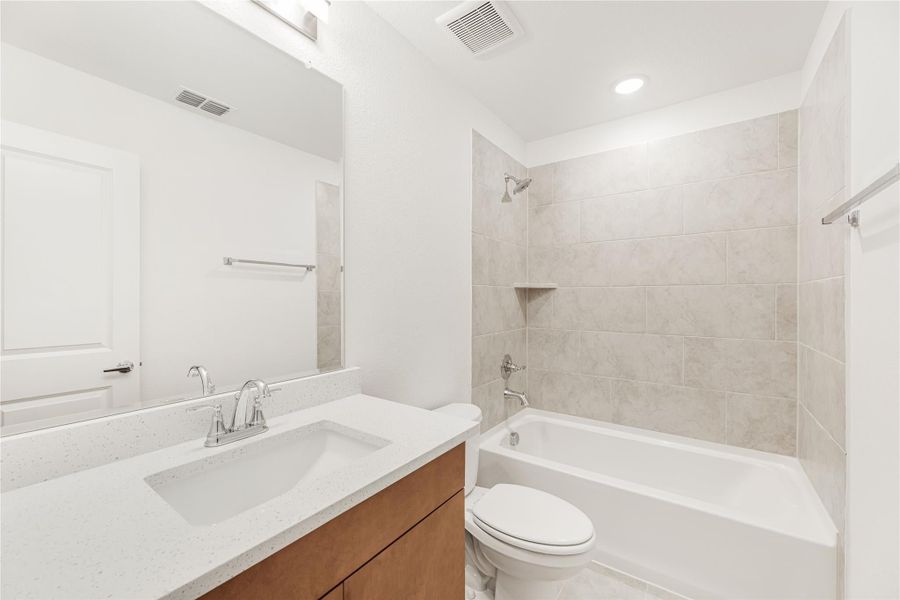 Bathroom with single vanity, white quartz countertop, tub-shower combo with beige tile surround, and toilet.