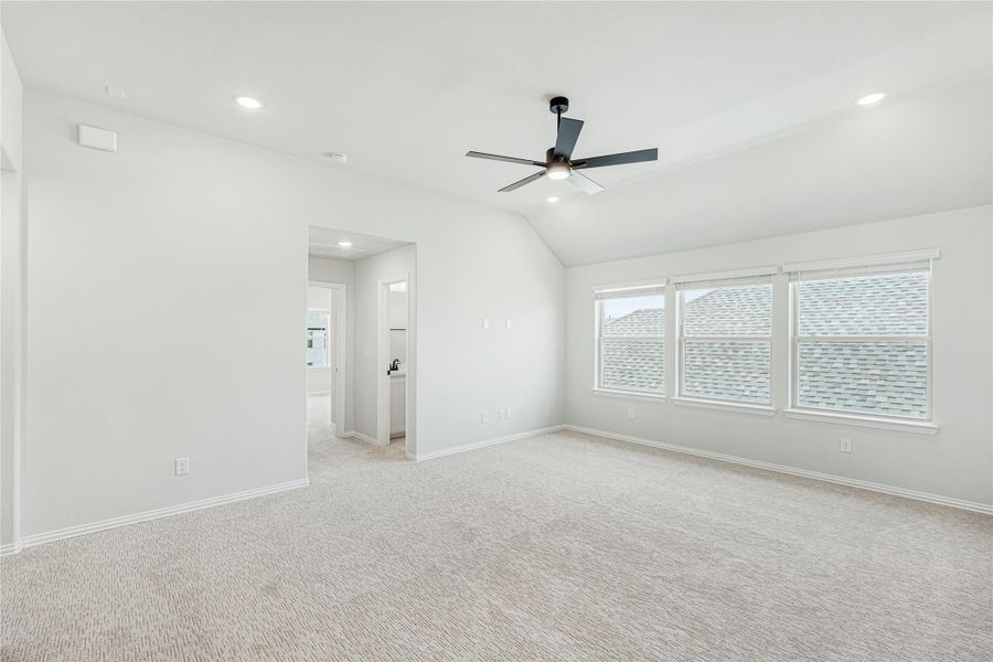 Spacious bedroom with vaulted ceiling, ceiling fan, carpet flooring, and large windows