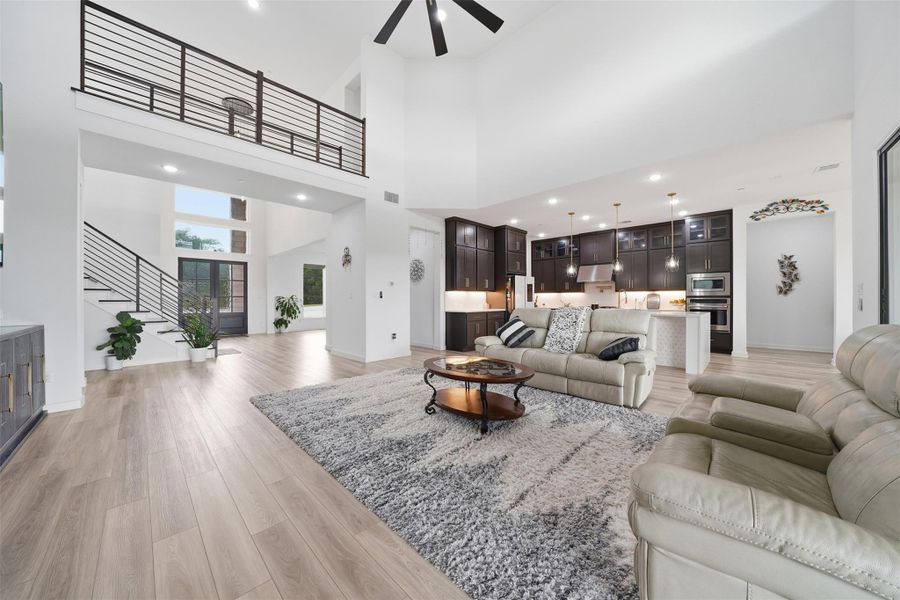 Spacious open concept living area featuring vaulted ceilings, light-toned flooring, and a modern kitchen with dark cabinetry and stainless steel appliances