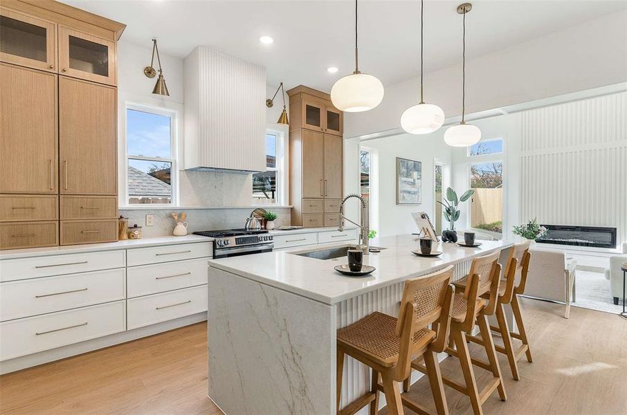 Kitchen featuring glass insert cabinets, a kitchen bar, light stone countertops, a center island with sink, and plenty of natural light