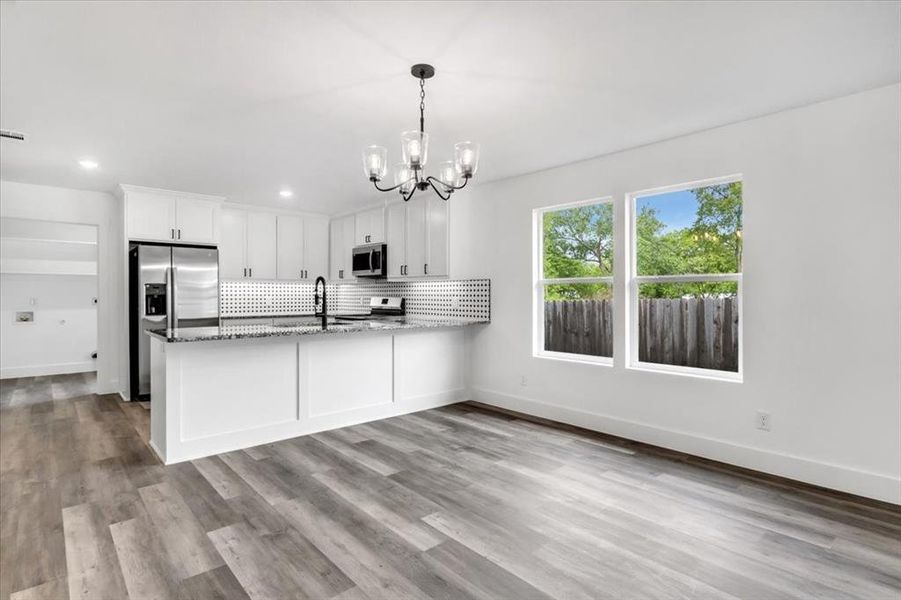 Kitchen with stainless steel appliances, white cabinetry, light hardwood / wood-style floors, and a notable chandelier