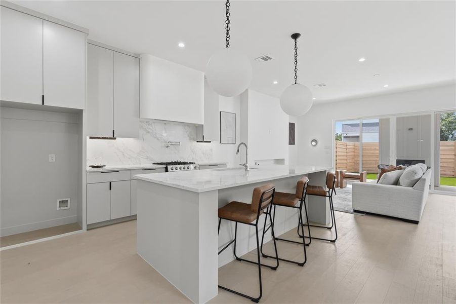 Contemporary kitchen featuring a large central island with seating, a gas range with a substantial range hood, under-cabinet lighting, and light wood-finish flooring