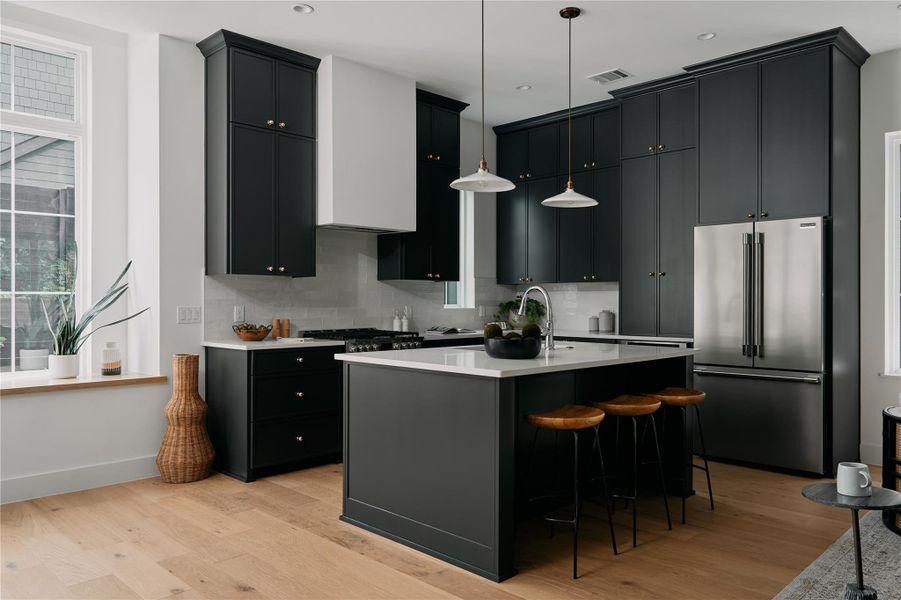 Kitchen with high end refrigerator, light wood-type flooring, backsplash, light countertops, and recessed lighting Kitchen with high end refrigerator, light wood-type flooring, backsplash, light countertops, and recessed lighting