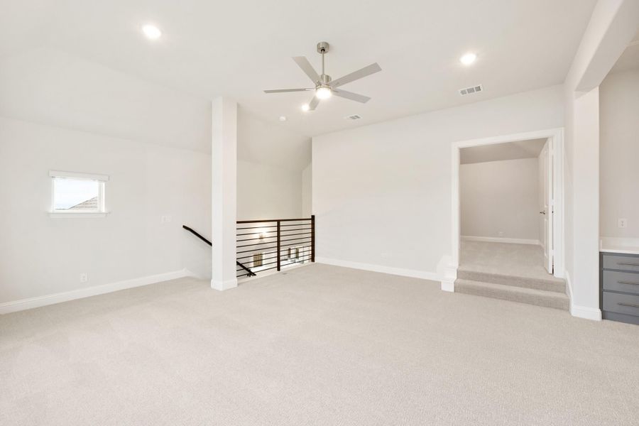 Spacious upstairs bonus room with carpet, ceiling fan, stair railing, and open closet area