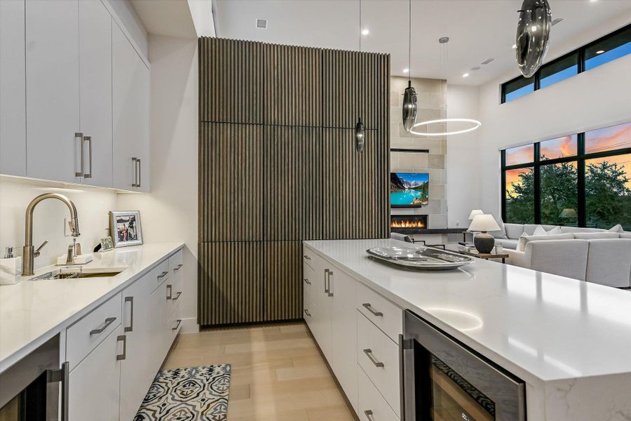 Kitchen featuring white cabinets, wine cooler, light wood-style floors, decorative light fixtures, and a high ceiling Kitchen featuring white cabinets, wine cooler, light wood-style floors, decorative light fixtures, and a high ceiling