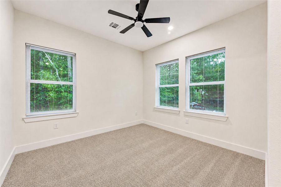 Bright and airy 2nd bedroom with plush carpet, large windows offering lush green views, and a sleek ceiling fan.
