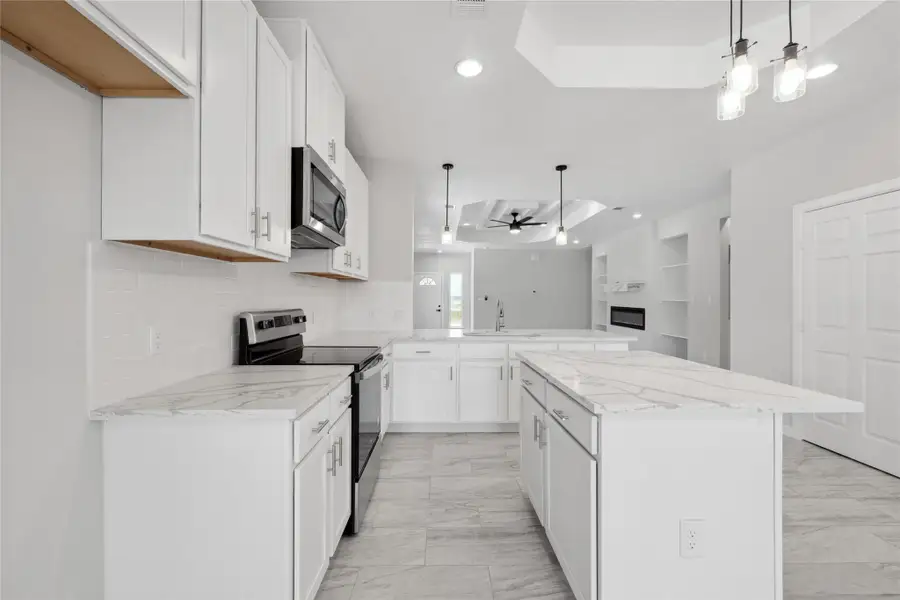 Kitchen featuring appliances with stainless steel finishes, a tray ceiling, a peninsula, a skylight, and light marble finish flooring Kitchen featuring appliances with stainless steel finishes, a tray ceiling, a peninsula, a skylight, and light marble finish flooring
