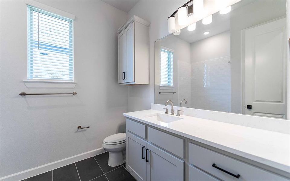 Spacious bathroom featuring a white vanity with an integrated sink, a large mirror, and dark tile flooring Spacious bathroom featuring a white vanity with an integrated sink, a large mirror, and dark tile flooring