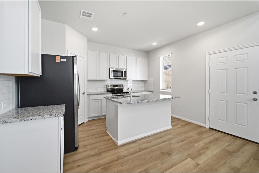 Kitchen featuring white cabinetry, light stone countertops, an island with sink, stainless steel appliances, and decorative backsplash