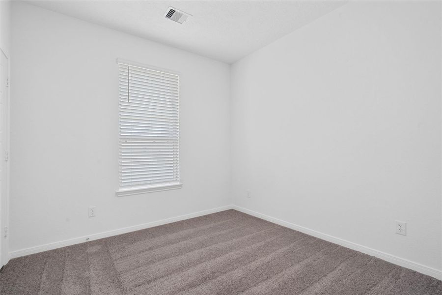 Tucked peacefully in the front of the home is this comfortable secondary bedroom which provides a quiet retreat for guests or family. It features plush carpet flooring, a large window with fitted privacy blinds, neutral tone paint, and an ample sized closet space.
