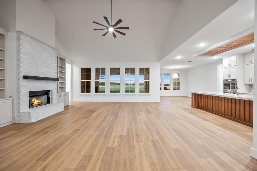 Unfurnished living room with light wood-type flooring, a brick fireplace, built in shelves, high vaulted ceiling, and a ceiling fan