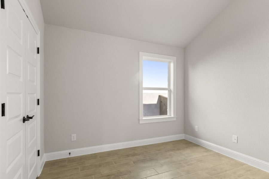 Image of a one story home bedroom with light wood-like flooring and light grey painted walls with a window in the corner Image of a one story home bedroom with light wood-like flooring and light grey painted walls with a window in the corner