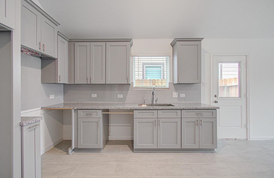 Sleek kitchen featuring modern gray cabinetry, granite countertops, and ample natural light, complemented by a convenient exterior door access.