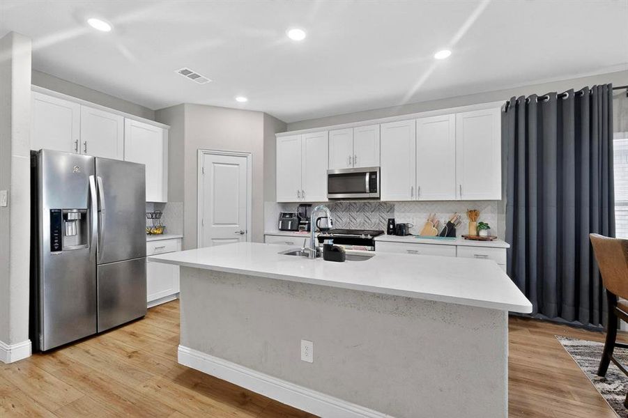 Kitchen featuring stainless steel appliances, white cabinets, light stone counters, an island with sink, and recessed lighting Kitchen featuring stainless steel appliances, white cabinets, light stone counters, an island with sink, and recessed lighting