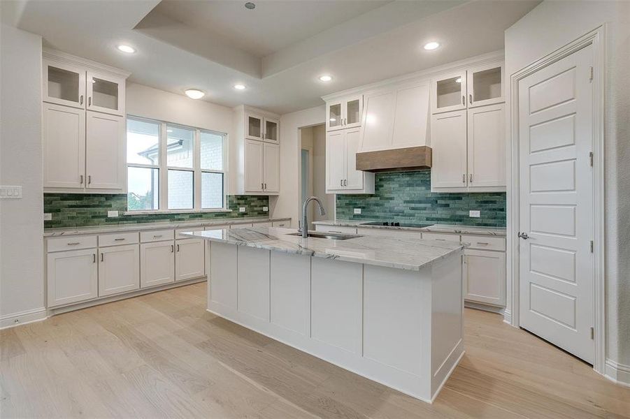 Kitchen featuring a center island with sink, white cabinets, decorative backsplash, sink, and light stone countertops