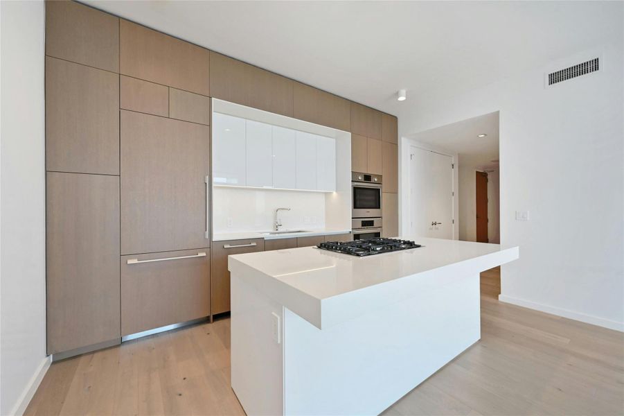 A streamlined culinary space highlighted by Bosch appliances, a gas cooktop built into the expansive quartz island, and custom cabinetry that seamlessly conceals the refrigerator and dishwasher for a clean, modern aesthetic.