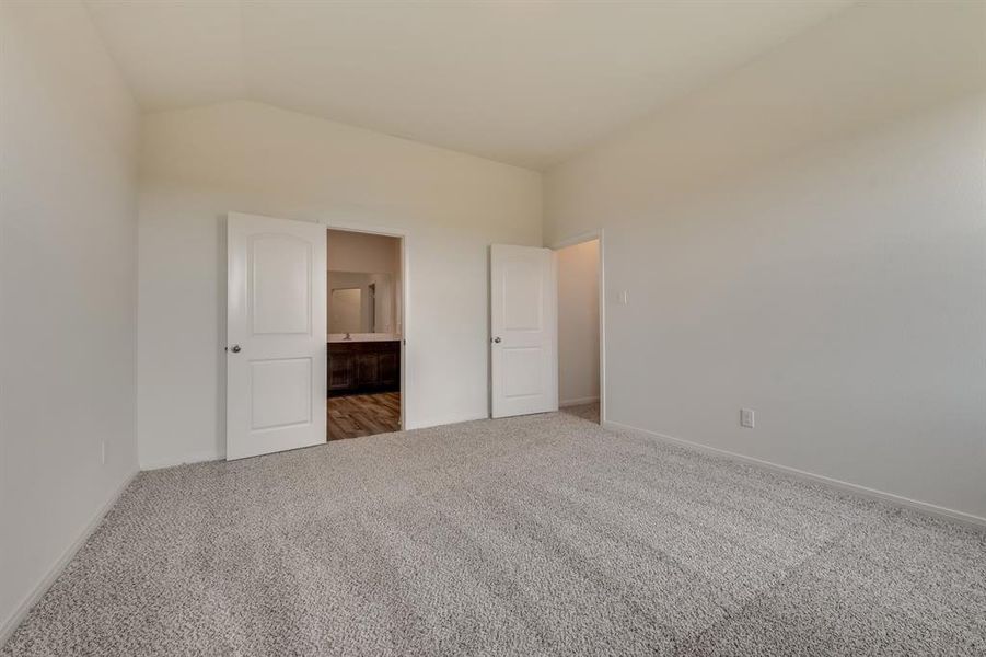 Unfurnished bedroom with carpet floors, ensuite bath, and vaulted ceiling