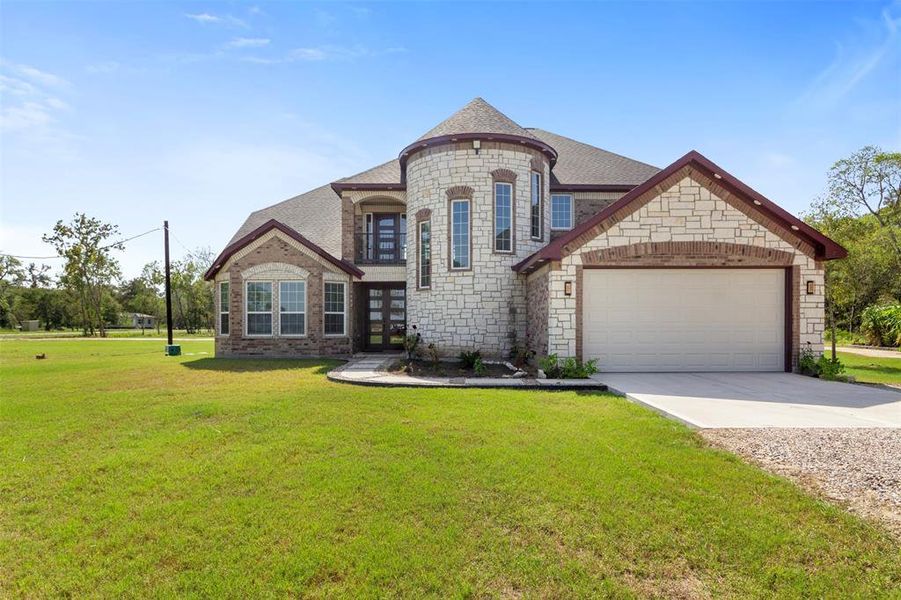 This charming home features a unique stone exterior with a turret design, large windows for natural light, and a spacious two-car garage. It is set on a generous green lawn, providing plenty of outdoor space.