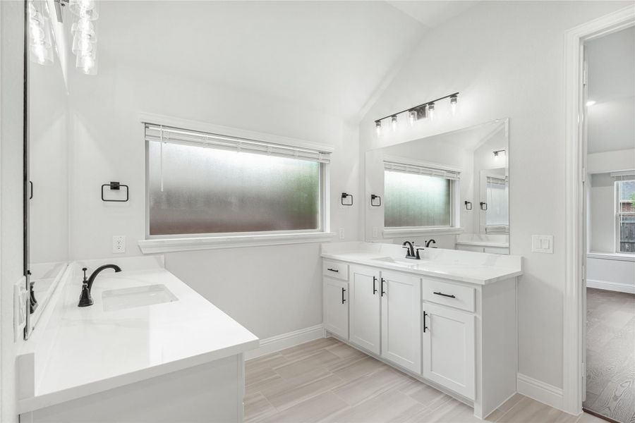 Master bathroom with dual sinks, white cabinets, soaking tub, and vaulted ceiling with frosted windows Master bathroom with dual sinks, white cabinets, soaking tub, and vaulted ceiling with frosted windows
