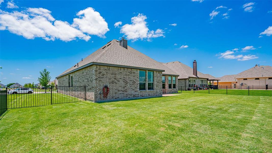 Expansive backyard featuring a large green lawn, full brick exterior, multiple windows, a covered patio, and a black metal fence