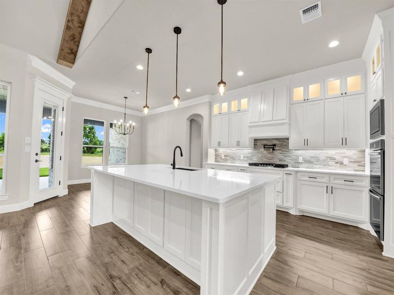 Kitchen with a sink, tasteful backsplash, a center island with sink, white cabinets, and ornamental molding Kitchen with a sink, tasteful backsplash, a center island with sink, white cabinets, and ornamental molding