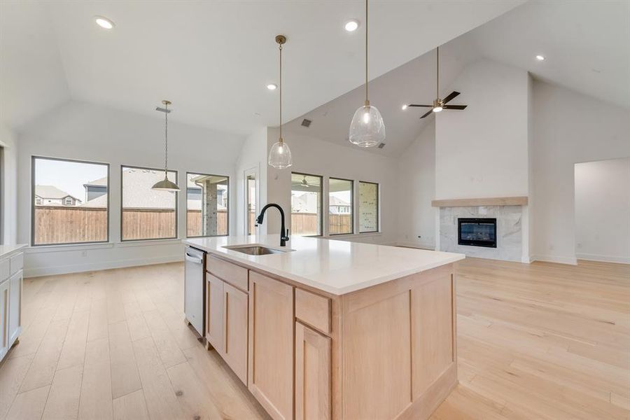 Kitchen with light brown cabinets, high vaulted ceiling, decorative light fixtures, light wood-type flooring, and a premium fireplace