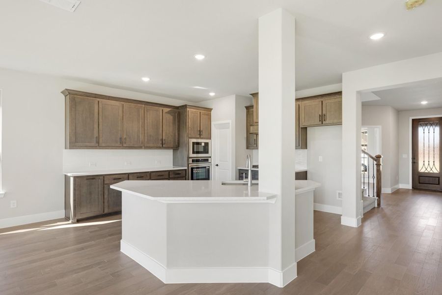 Open kitchen with brown wood cabinets, white island, stainless appliances, and hardwood floors