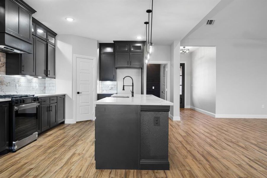 Kitchen featuring pendant lighting, backsplash, a center island with sink, sink, and stainless steel range