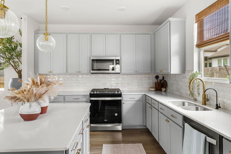 Kitchen featuring stainless steel appliances, light stone counters, dark wood-type flooring, gray cabinets, and decorative backsplash