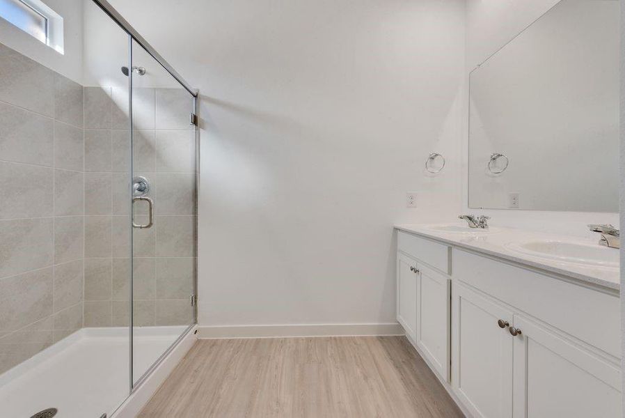 Bathroom featuring double vanity, a stall shower, and wood finished floors Bathroom featuring double vanity, a stall shower, and wood finished floors