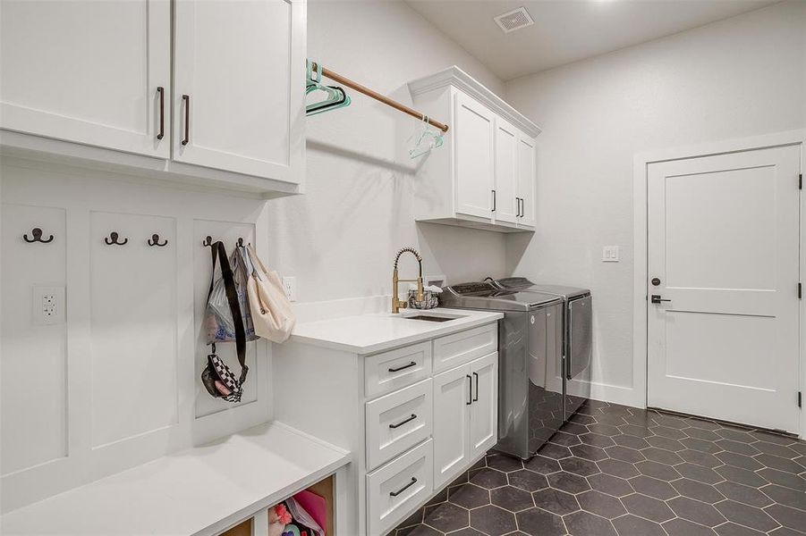 Clothes washing area featuring sink, washer and clothes dryer, and cabinets