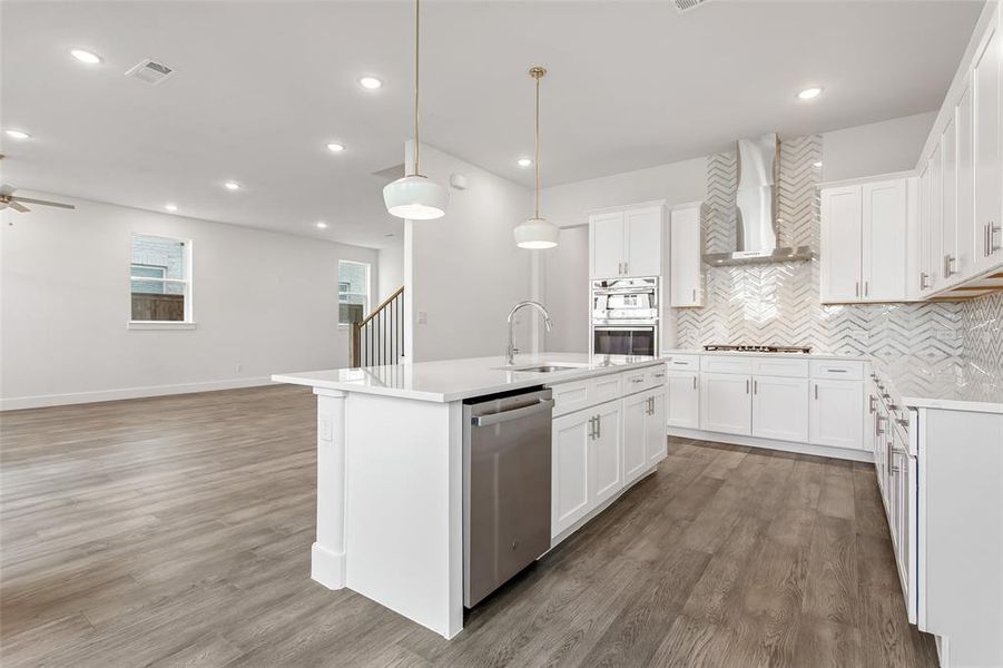 Kitchen featuring sink, wall chimney exhaust hood, an island with sink, white cabinetry, and stainless steel appliances